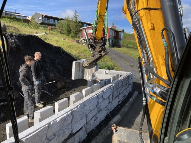 Excavator lifting MagnumStone retaining wall gravity extender