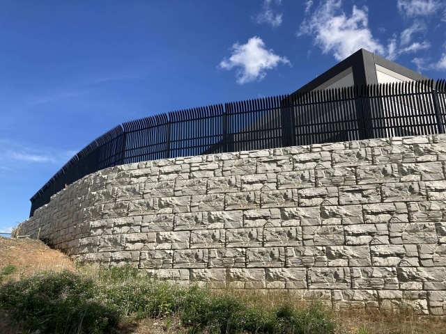 MagnumStone curved retaining wall with fence atop for commercial project.