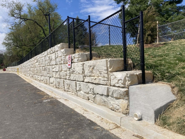 School retaining wall with top of wall fence installation.