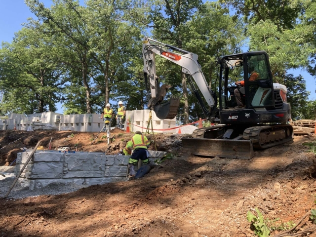 Compact Excavator lifting MagnumStone block.